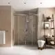 Dusche mit gläsernen Schiebetüren, blatt geformter Duschkopf und Handbrause, Wand mit braunem Putz, Holzregal mit dekorativen Elementen. Ideal Standard Badearmatur sichtbar.